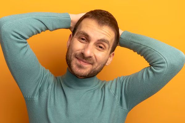 giovane uomo sorridente che guarda avanti mettendo le mani dietro la testa