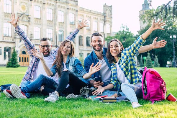 quattro studenti seduti sull'erba che salutano felicemente