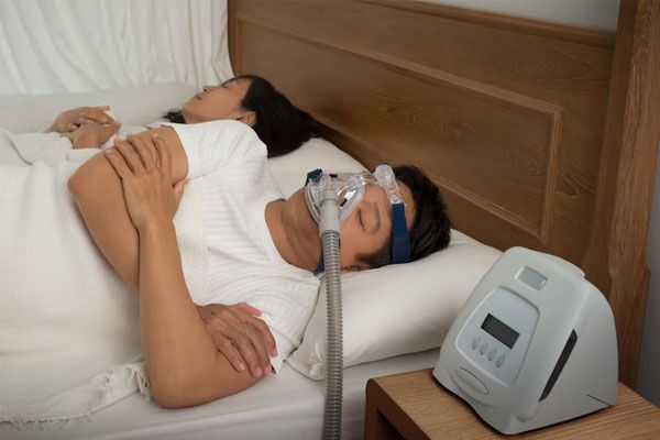 uomo con maschera CPAP mentre soffre di apnea notturna e donna a letto
