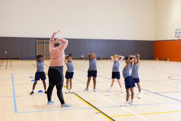 Diversi bambini fanno stretching con un insegnante durante la lezione di educazione fisica in una palestra.