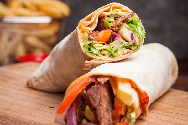 Vista laterale di shawarma con patatine fritte su un tagliere da cucina