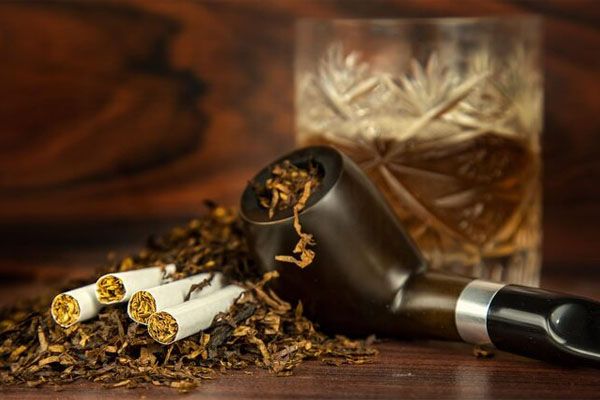 Foto di una pipa e sigari con un bicchiere di liquore e tabacco essiccato