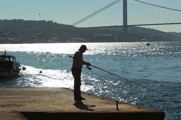 Uomo che pesca in un porto con il ponte sul Bosforo sullo sfondo