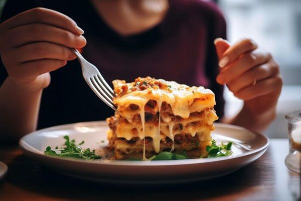 Primo piano di un piatto di lasagne e di una mano con una forchetta