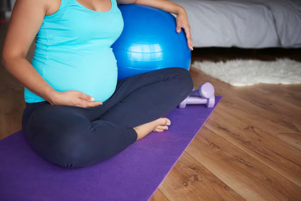 Donna incinta in abbigliamento sportivo seduta su un tappetino accanto ad attrezzature sportive