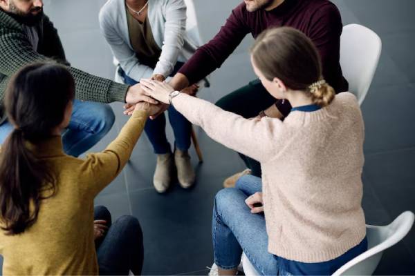 Persone sedute e che si tengono per mano in un gruppo di auto-aiuto